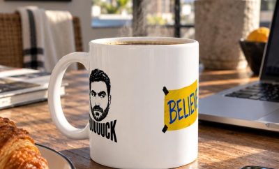 White ceramic mug with the Roy-inspired face graphic and yellow BELIEVE sign in a morning setting